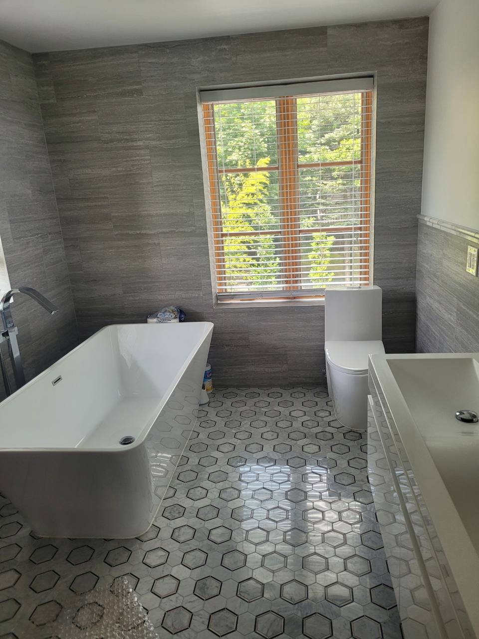 Grey stone bath with hex mosaic floor and freestanding tub